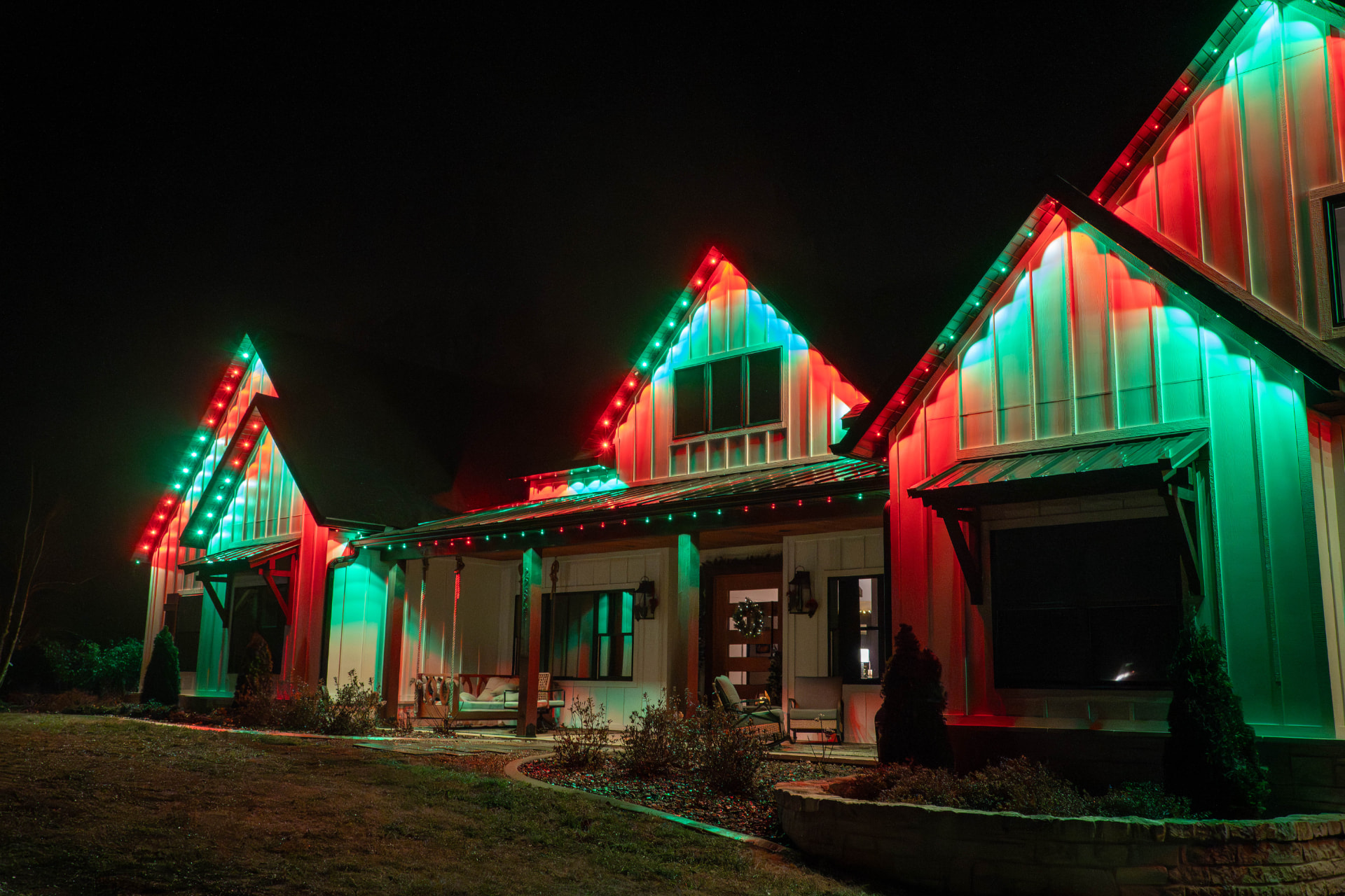 Modern farmhouse illuminated with red and green holiday lights